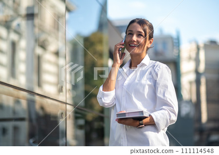 Pretty businessman with the phone and notebook in hands in the street Pretty businessman with the phone and notebook in hands in the street 111114548