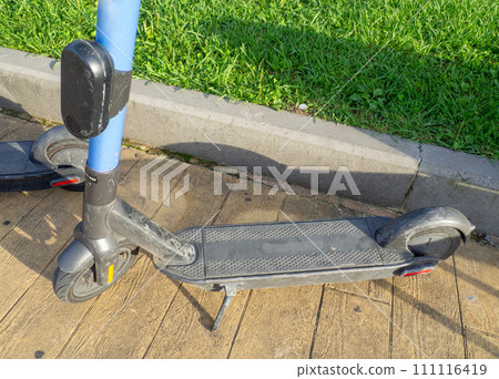 A used scooter is parked on the sidewalk. Part of a scooter close-up. Leisure. Movement on two-wheeled transport. A used scooter is parked on the sidewalk. Part of a scooter close-up. Leisure. Movement on two-wheeled transport. 111116419