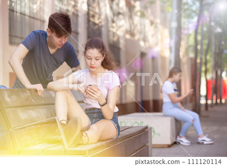 Two teenagers using smartphones sitting on bench Two teenagers using smartphones sitting on bench 111120114
