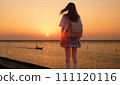 A girl looking at the sunset over the embankment and the fishing boats returning to the port. A combination of live action and AI generation. (The focus is on the sunset and the seaweed trellis.) 111120116