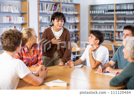 Asian schoolgirl talking in front of team of schoolkids during classes in library Asian schoolgirl talking in front of team of schoolkids during classes in library 111120484