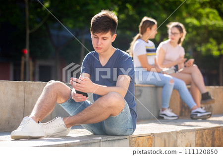 Teen guy plays on smartphone on street Teen guy plays on smartphone on street 111120850