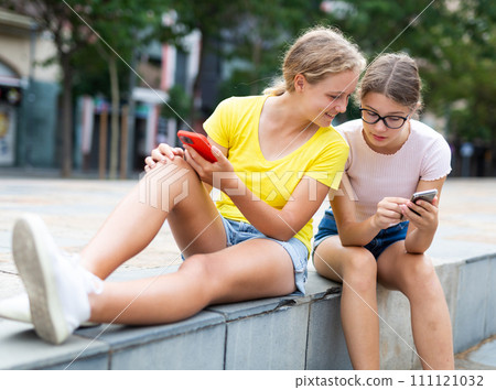 Youth girls with smartphones sitting in square 111121032