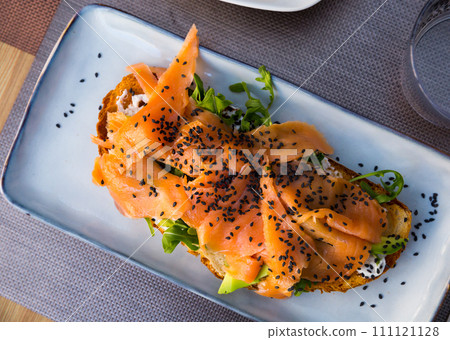 Delicious smoked salmon with arugula avocado and seeds on fried bread Delicious smoked salmon with arugula avocado and seeds on fried bread 111121128