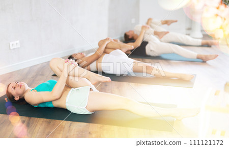 Groupd og young people doing reclining twist yoga pose in studio. 111121172