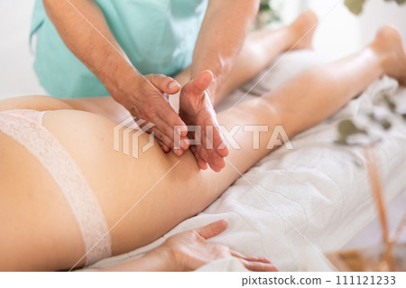 Woman covered with white towel lies and enjoys during anti-cellulite massage in hips and legs 111121233