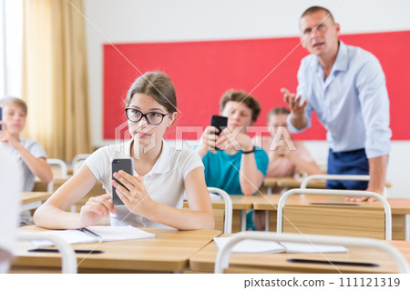 Teen girl student using smartphone while studying in college Teen girl student using smartphone while studying in college 111121319