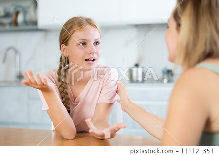 Cheerful teenage girl chatting friendly to mother in home kitchen Cheerful teenage girl chatting friendly to mother in home kitchen 111121351