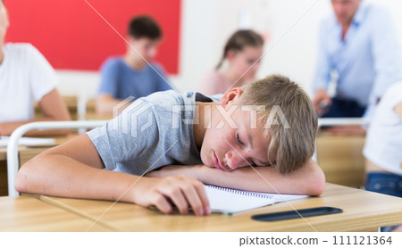 Tired teen student sleeping at desk during lesson Tired teen student sleeping at desk during lesson 111121364