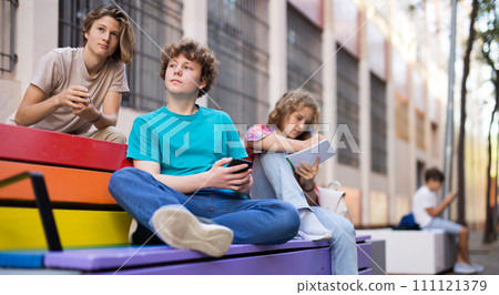 Schoolchildren sitting on bench in schoolyard 111121379