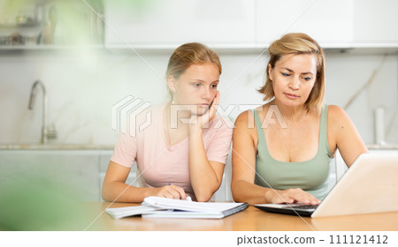 Mother assisting teenage daughter doing school assignment at home Mother assisting teenage daughter doing school assignment at home 111121412