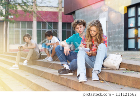 Teenage boy and girl sitting on steps near school 111121562