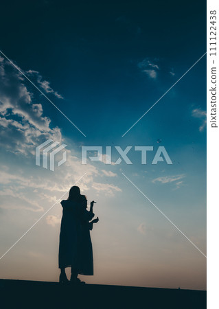 Silhouette of a young woman blowing soap bubbles against the sunset background 111122438