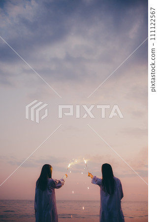 Silhouette of a young woman lighting fireworks against the sunset background 111122567
