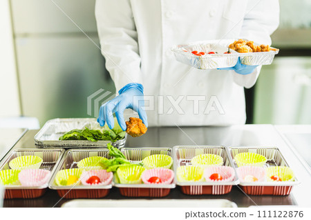 Young woman packing side dishes at a food factory, faceless 111122876