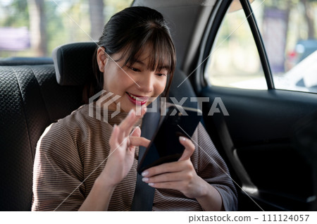 A happy young Asian female passenger is using her smartphone in a taxi, chatting with someone. A happy young Asian female passenger is using her smartphone in a taxi, chatting with someone. 111124057