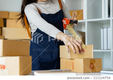 Young business entrepreneur sealing a box with tape. Preparing for shipping, Packing, online selling, e-commerce concept Young business entrepreneur sealing a box with tape. Preparing for shipping, Packing, online selling, e-commerce concept 111124759
