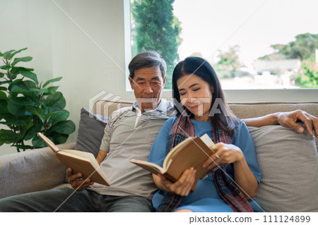 Retired elderly couple sits on couch in their home reading relaxing book. Senior Activity Concept Retired elderly couple sits on couch in their home reading relaxing book. Senior Activity Concept 111124899
