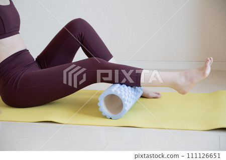 Young woman massaging legs with home roller Young woman massaging legs with home roller 111126651