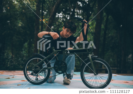 Young handsome bearded man taking a break while travelling the city with his bicycle using his digital tablet looking away thoughtfully Young handsome bearded man taking a break while travelling the city with his bicycle using his digital tablet looking away thoughtfully 111128127