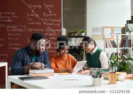 Group of three African American teenagers enjoying work together in college classroom and using digital tablet Group of three African American teenagers enjoying work together in college classroom and using digital tablet 111129136