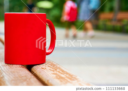 Red ceramic cup on a wooden bench in the park 111133668