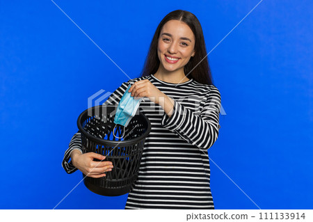 Woman throwing out surgical medical protective mask into bin after pandemic illness sickness ending 111133914