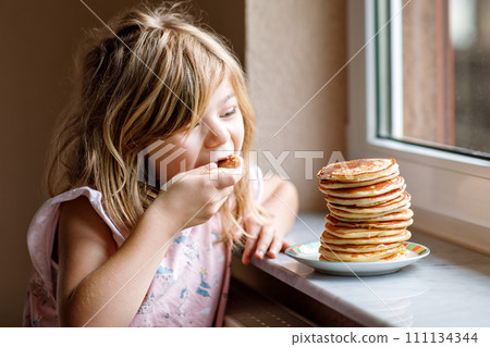 Little happy preschool girl with a large stack of pancakes for breakfast. Positive child eating healthy homemade food in the morning. 111134344