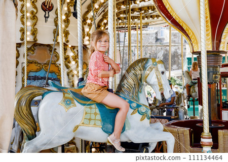 Happy positive preschool girl having a ride on the old vintage merry-go-round in city of St Malo France. Smiling child on a horse. 111134464