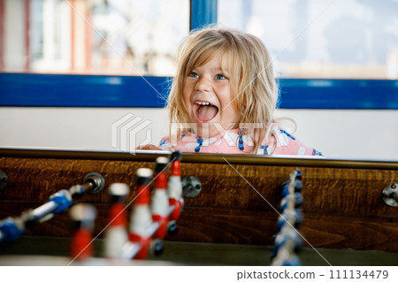 Little preschool girl playing table soccer. Happy excited positive child having fun with family game with siblings or friends. Little preschool girl playing table soccer. Happy excited positive child having fun with family game with siblings or friends. 111134479