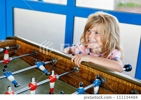 Little preschool girl playing table soccer. Happy excited positive child having fun with family game with siblings or friends. Little preschool girl playing table soccer. Happy excited positive child having fun with family game with siblings or friends. 111134484