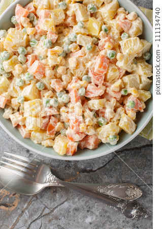 Delicious Brazilian gaucho salad with potatoes, green peas, carrots, corn and apple covered with mayonnaise close-up on a plate. Vertical top view Delicious Brazilian gaucho salad with potatoes, green peas, carrots, corn and apple covered with mayonnaise close-up on a plate. Vertical top view 111134740