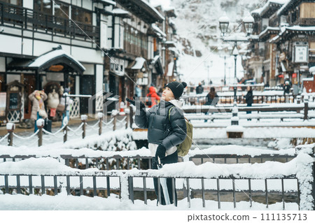 Woman tourist Visiting Ginzan Onsen in Yamagata, happy Traveler sightseeing Japanese Onsen village with Snow in winter season. landmark and popular for attraction in Japan. Travel and Vacation concept Woman tourist Visiting Ginzan Onsen in Yamagata, happy Traveler sightseeing Japanese Onsen village with Snow in winter season. landmark and popular for attraction in Japan. Travel and Vacation concept 111135713