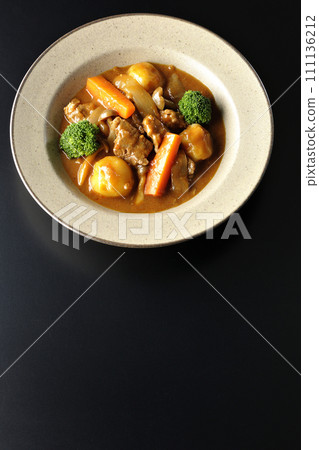 An overhead shot of beef stew with many ingredients such as broccoli, carrots, and shimeji mushrooms against a black background 111136212
