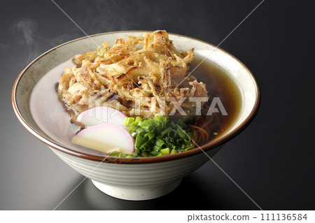 Hot kakiage soba or tempura soba topped with kamaboko and green onions photographed against a black background 111136584