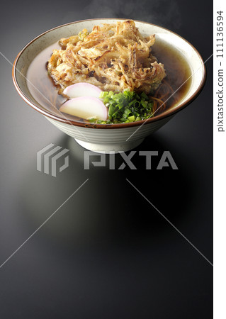 Hot kakiage soba or tempura soba topped with kamaboko and green onions photographed against a black background Hot kakiage soba or tempura soba topped with kamaboko and green onions photographed against a black background 111136594