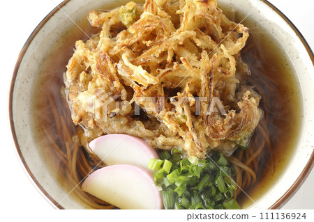 An overhead shot of piping hot kakiage soba or tempura soba topped with fish cake and onions against a white background 111136924