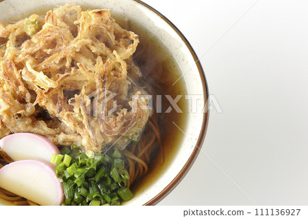 An overhead shot of piping hot kakiage soba or tempura soba topped with fish cake and onions against a white background 111136927