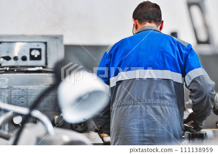 Portrait of professional turner at work on lathe in workshop. 50-55 year old turner in overalls and 111138959