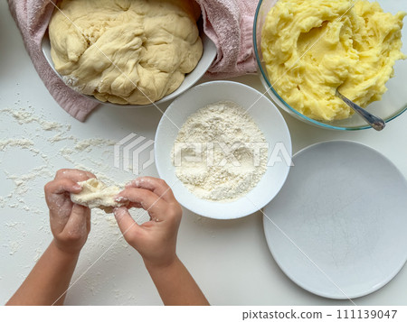 The hands of child knead the dough for making pies on white table, top view. 111139047
