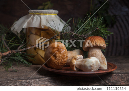 Clay plate with three porcini mushrooms commonly known as Boletus Edulis and glass jar with canned mushrooms on vintage wooden background.. Clay plate with three porcini mushrooms commonly known as Boletus Edulis and glass jar with canned mushrooms on vintage wooden background.. 111139834