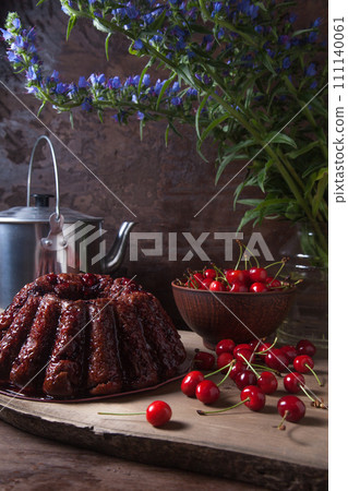Delicious chocolate cake with sweet cherry, vintage kettle and bouquet of blue flowers on dark wooden background.. Delicious chocolate cake with sweet cherry, vintage kettle and bouquet of blue flowers on dark wooden background.. 111140061