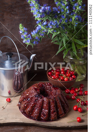 Delicious chocolate cake with sweet cherry, vintage kettle and bouquet of blue flowers on dark wooden background.. Delicious chocolate cake with sweet cherry, vintage kettle and bouquet of blue flowers on dark wooden background.. 111140062
