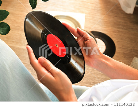 Vinyl records on a wooden table. The girl's hand examines vinyl records. Retro style. Sound technology for DJ to mix and play music. Black vinyl record. 111140128