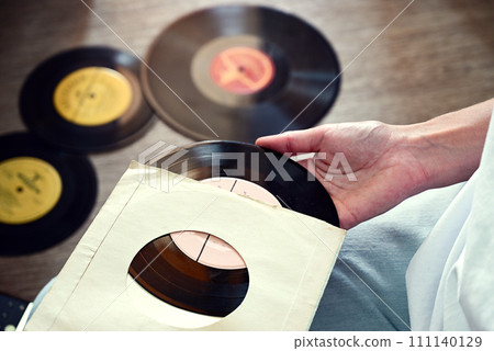Vinyl records on a wooden table. The girl's hand examines vinyl records. Retro style. Sound technology for DJ to mix and play music. Black vinyl record. Vinyl records on a wooden table. The girl's hand examines vinyl records. Retro style. Sound technology for DJ to mix and play music. Black vinyl record. 111140129