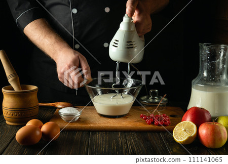 Delicious and healthy breakfast from the chef in the kitchen. Making egg omelet with milk and eggs using a hand-held electric mixer 111141065