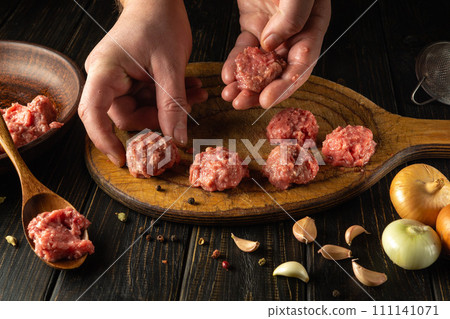 The cook hand places a raw meat cutlet on the kitchen board. Cooking meat on the kitchen table for breakfast. Cooking recipes and restaurant food concept 111141071