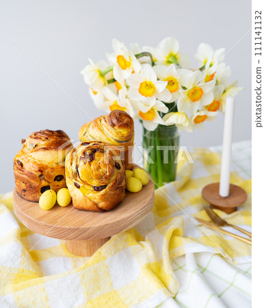 Freshly baked pastries, yellow candies, and white daffodils on a checkered cloth. A beautiful springtime table setting. Easter holiday concept. Freshly baked pastries, yellow candies, and white daffodils on a checkered cloth. A beautiful springtime table setting. Easter holiday concept. 111141132