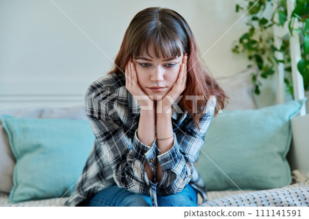 Upset sad young female sitting on couch at home Upset sad young female sitting on couch at home 111141591