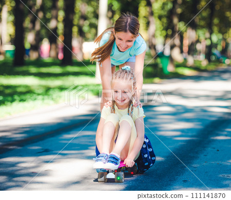 Smiling kids joyfully riding on skateboard in sunshine park Smiling kids joyfully riding on skateboard in sunshine park 111141870